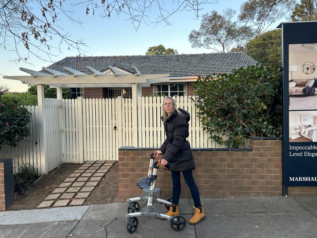 Emma standing outside her new home with her walking frame